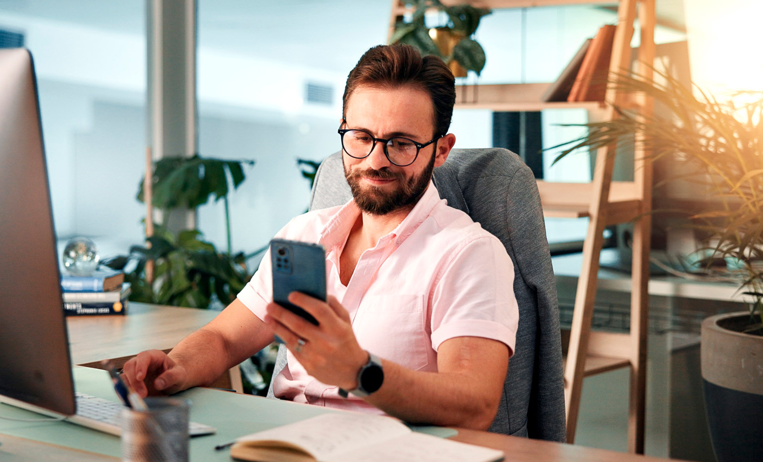 homem sentado à secretária a mexer em smartphone