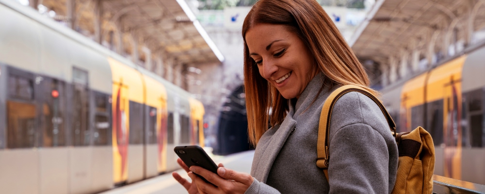 mulher sorridente a olhar para telemóvel em estação de comboios